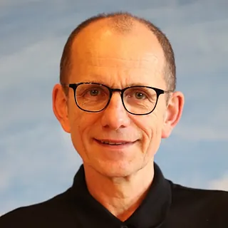 Ein Foto von Pastor.auf Zeit Dr. Tomáš Vočka. Er trägt ein schwarzes Hemd und eine Brille mit dunklem Rand.