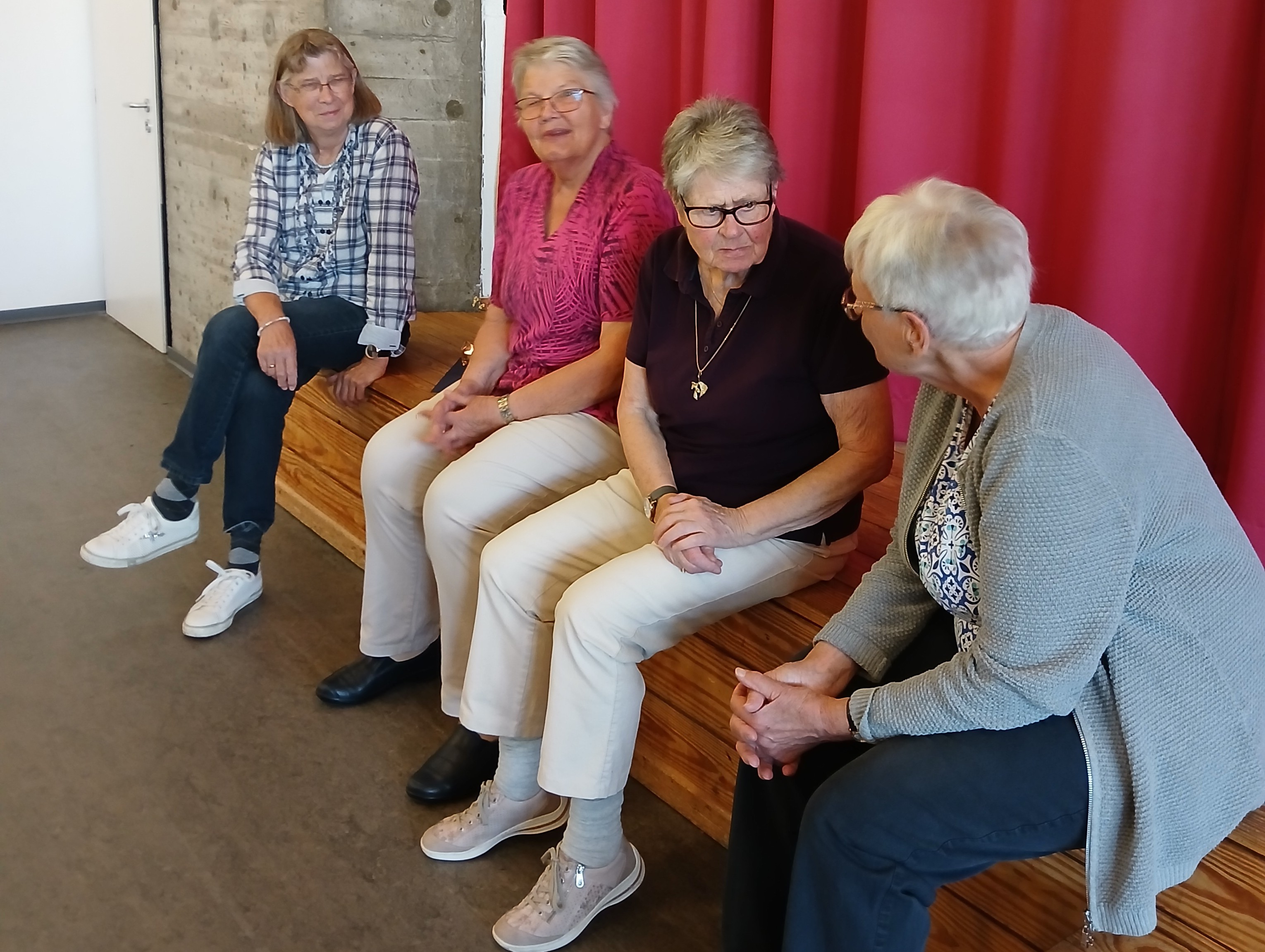 Eine Gruppe älterer Frauen sitzt nebeneinader auf einer Bank und unterhält sich.