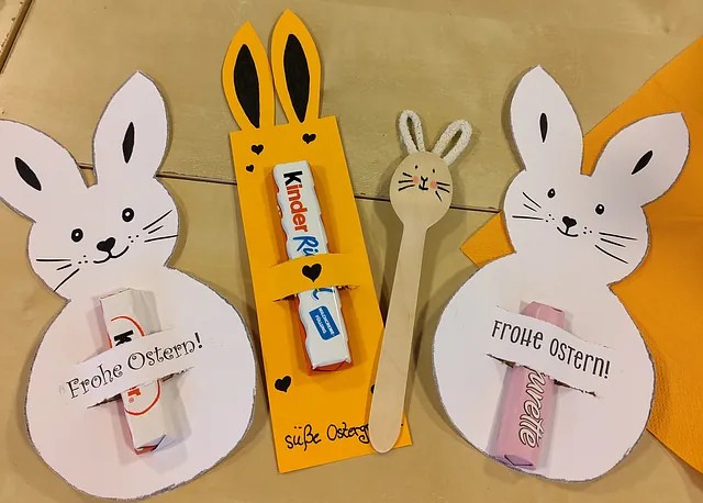 Foto von gebastelten Hasen, in denen Schokoriegel stecken. Daneben ein Hase aus einem Holzlöffel.