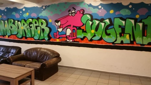 Ein Bild von einem bunten Graffiti an der Wand, davor stehen gemütliche Sofas.