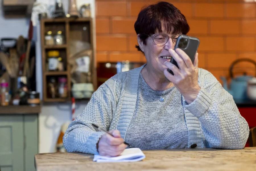 Das Bild eines Mannes und einer Frau, beide mit Sonnenbrillen und älter, die auf ein rotes Smartphone schauen.