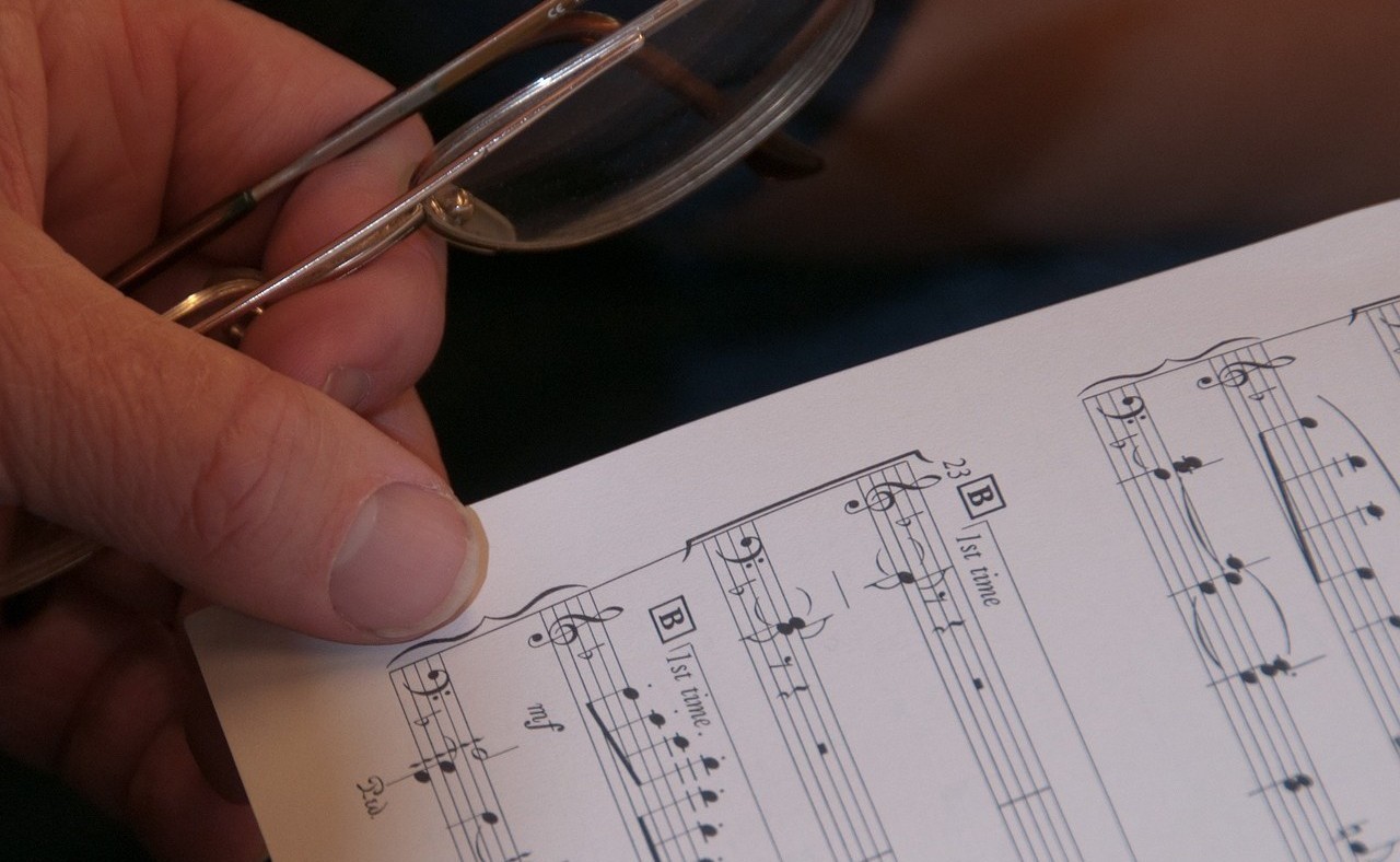 Eine Hand hält ein Notenblatt und eine Brille.