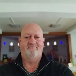 Ein Foto von Norbert Meyer. Er steht vor bunten Fenstern und blickt freundlich in die Kamera.