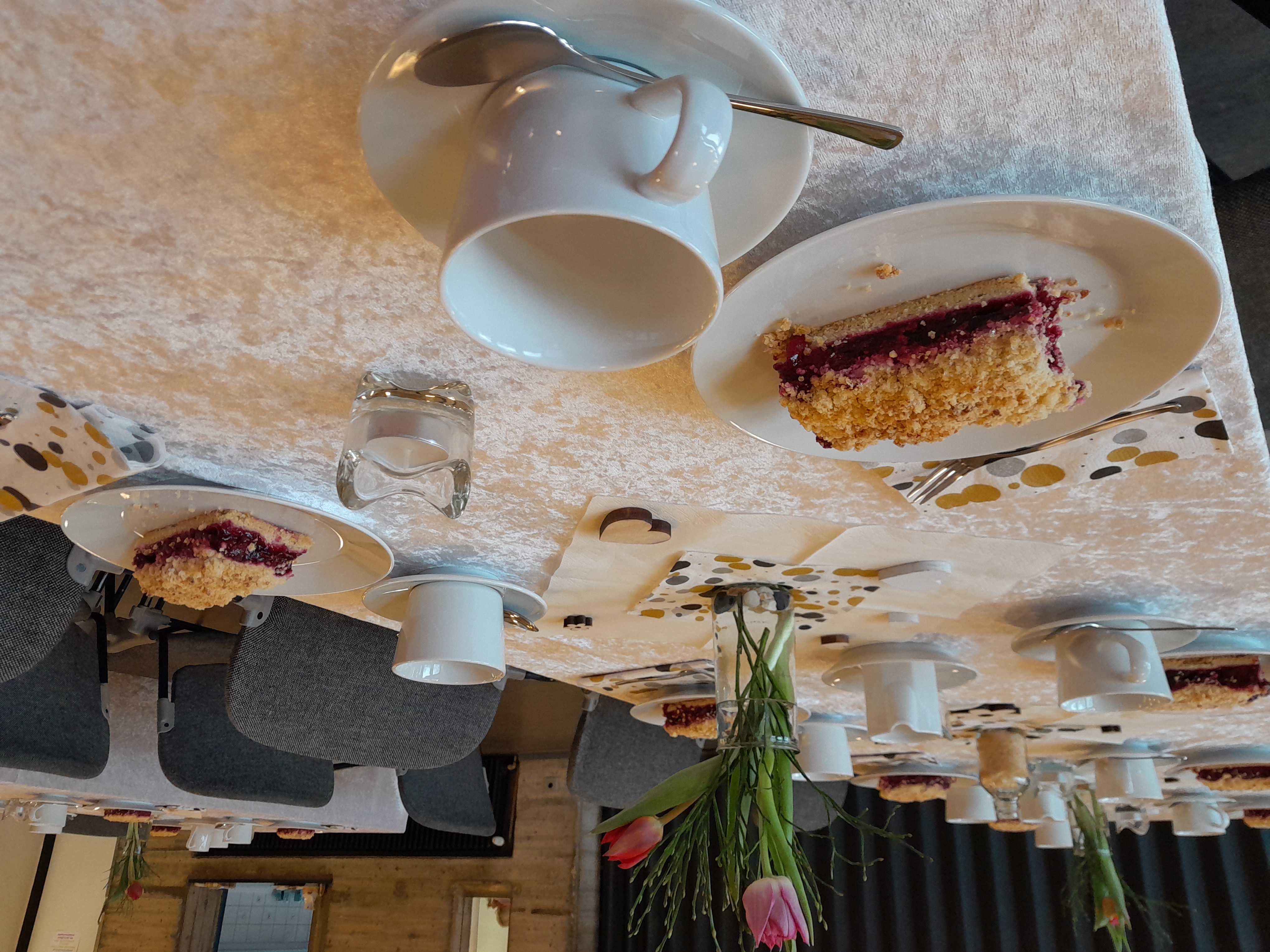 Ein Tisch ist als Kaffeetafel mit Geschirr und Kuchen gedeckt. Es stehen Blumen und Kerzen auf dem Tisch.