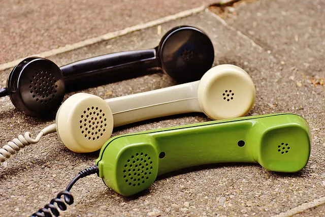 Auf dem Bild sind drei alte Telefonhörer zu sehen, die noch durch ein Kabel mit einem Telefonapparat verbunden sind.